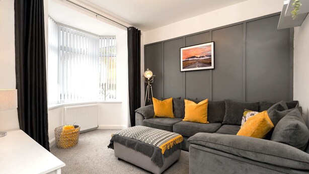 Een moderne woonkamer met een grijze bank, een bijpassend voetenbankje en een vloerlamp.