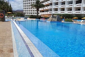 Relax by the pool surrounded by lounge chairs and umbrellas, with a rock feature in the center.