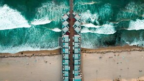 Vista aérea de un muelle con hileras de habitaciones que se adentran en el océano, rodeado de olas.