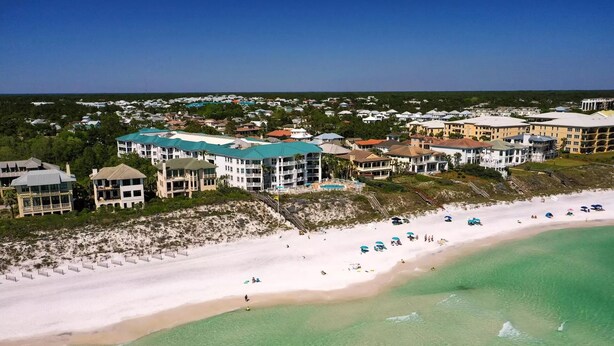 Ein Luftbild eines Küstenresorts mit Strandhäusern, einem Sandstrand und einem klaren, blauen Himmel.