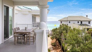 Ein Balkon mit Tisch und Stühlen, der Blick auf einen Strand und ein Gebäude bietet.