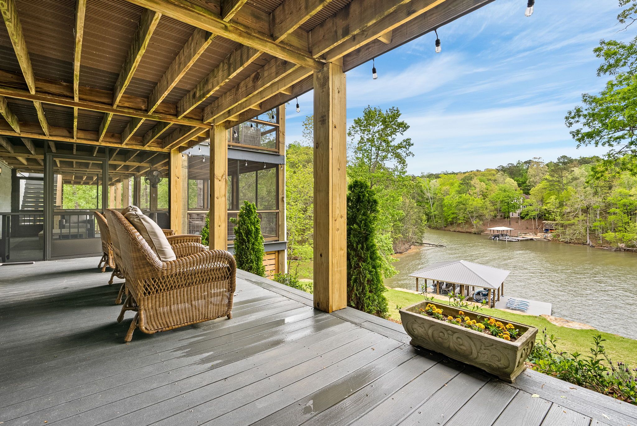 A wooden deck with wicker furniture and a planter, overlooking a river and greenery.