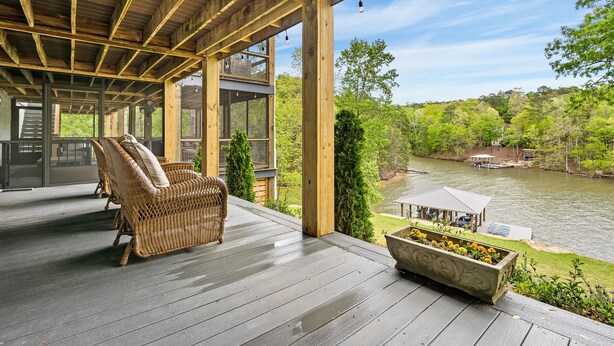 Terraza de madera con mobiliario de mimbre y una jardinera, con vista a un río y follaje.