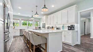 Una cocina moderna con armarios blancos, una isla grande, taburetes de bar e iluminación colgante.