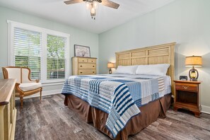 A bedroom with a large bed, wooden headboard, two bedside tables with lamps, a nightstand, a chair, and a dresser.