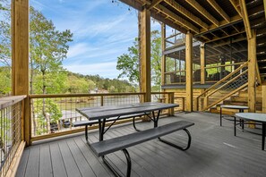 A wooden deck with picnic tables and a staircase leading to an upper level.