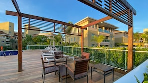 A rooftop terrace with wooden furniture, a pergola, and a view of residential buildings.