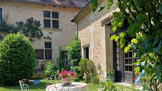 A stone building with a garden patio featuring a table and chairs. - Gîte de Charme en Pleine Nature (Champcevinel)