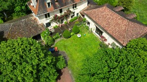 An aerial view of a large, two-story house with a red-tiled roof, surrounded by lush greenery and a well-maintained lawn. - Gîte de Charme en Pleine Nature (Champcevinel)
