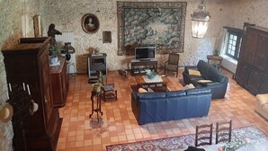 A rustic living room with a stone wall, a large painting, a blue sofa, and a television. - Gîte de Charme en Pleine Nature (Champcevinel)