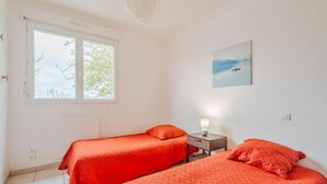 Una habitación con dos camas, una ventana, una mesita de noche con lámpara y un cuadro en la pared.