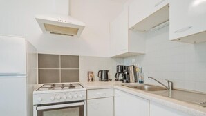 Cocina compacta con armarios blancos, estufa, lavamanos y cafetera.
