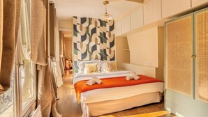 A hotel room with a bed, a large window with curtains, a patterned wall, and a rattan wardrobe. - Le Marais - Les Halles Colorful & Modern 3BD (Paris)