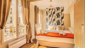 A hotel room with a bed, curtains, a window with a view, a radiator, and a patterned wall. - Le Marais - Les Halles Colorful & Modern 3BD (Paris)