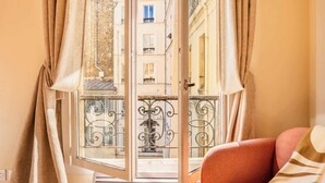 A room with a view through a window, a radiator, a patterned floor, and a red chair. - Le Marais - Les Halles Colorful & Modern 3BD (Paris)
