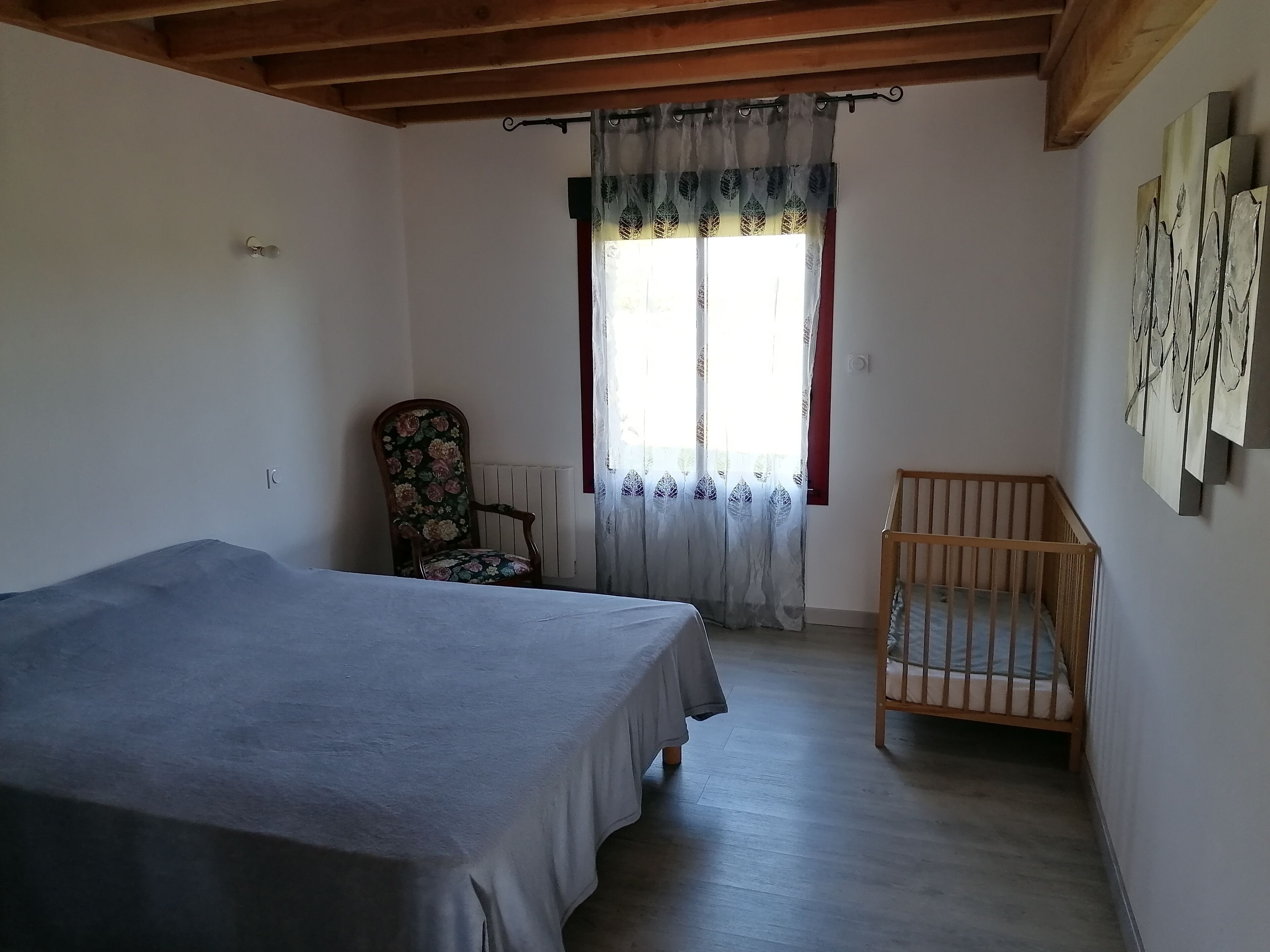 Ein Schlafzimmer mit Bett, Stuhl, einem Fenster mit Vorhängen und einem Heizkörper.