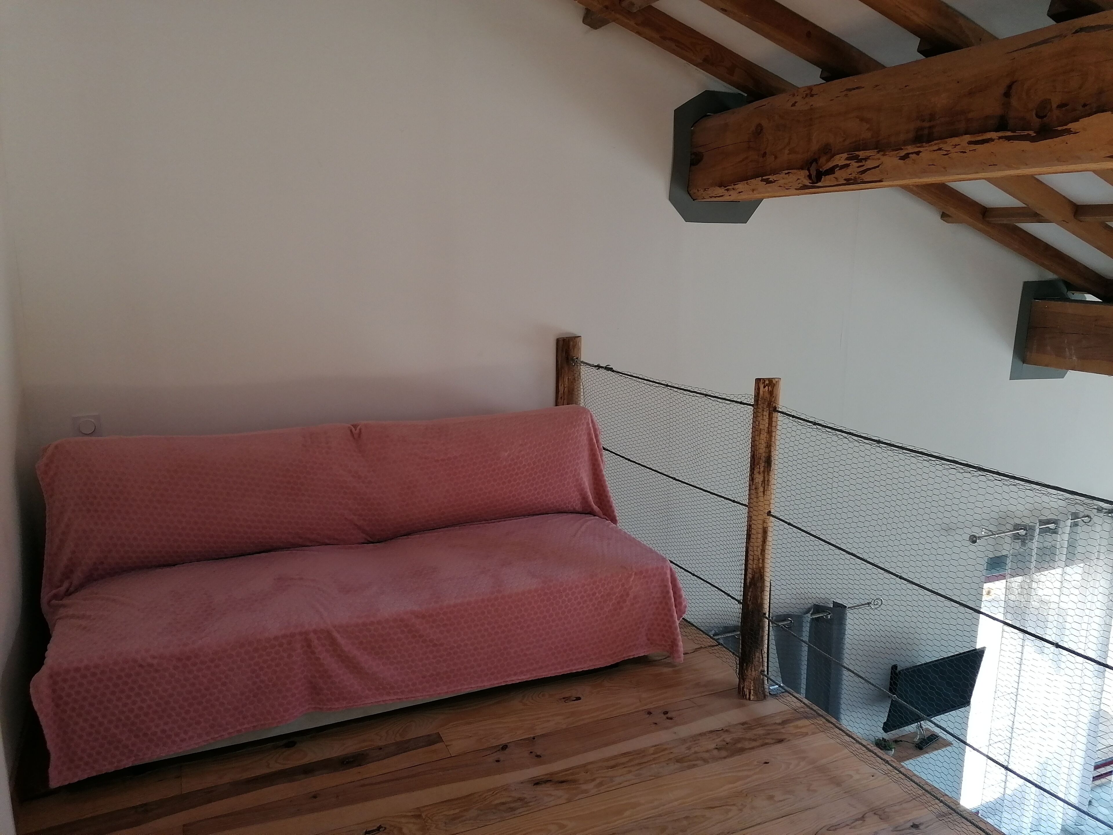 A wooden staircase with a mesh railing leading to a room with a pink sofa.