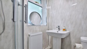 Un baño con cabina de ducha de vidrio, un radiador blanco, un lavabo con dispensador de jabón y un inodoro.
