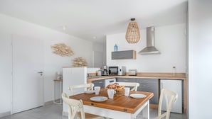 Une cuisine moderne avec des meubles blancs, une table à manger en bois et un luminaire suspendu.