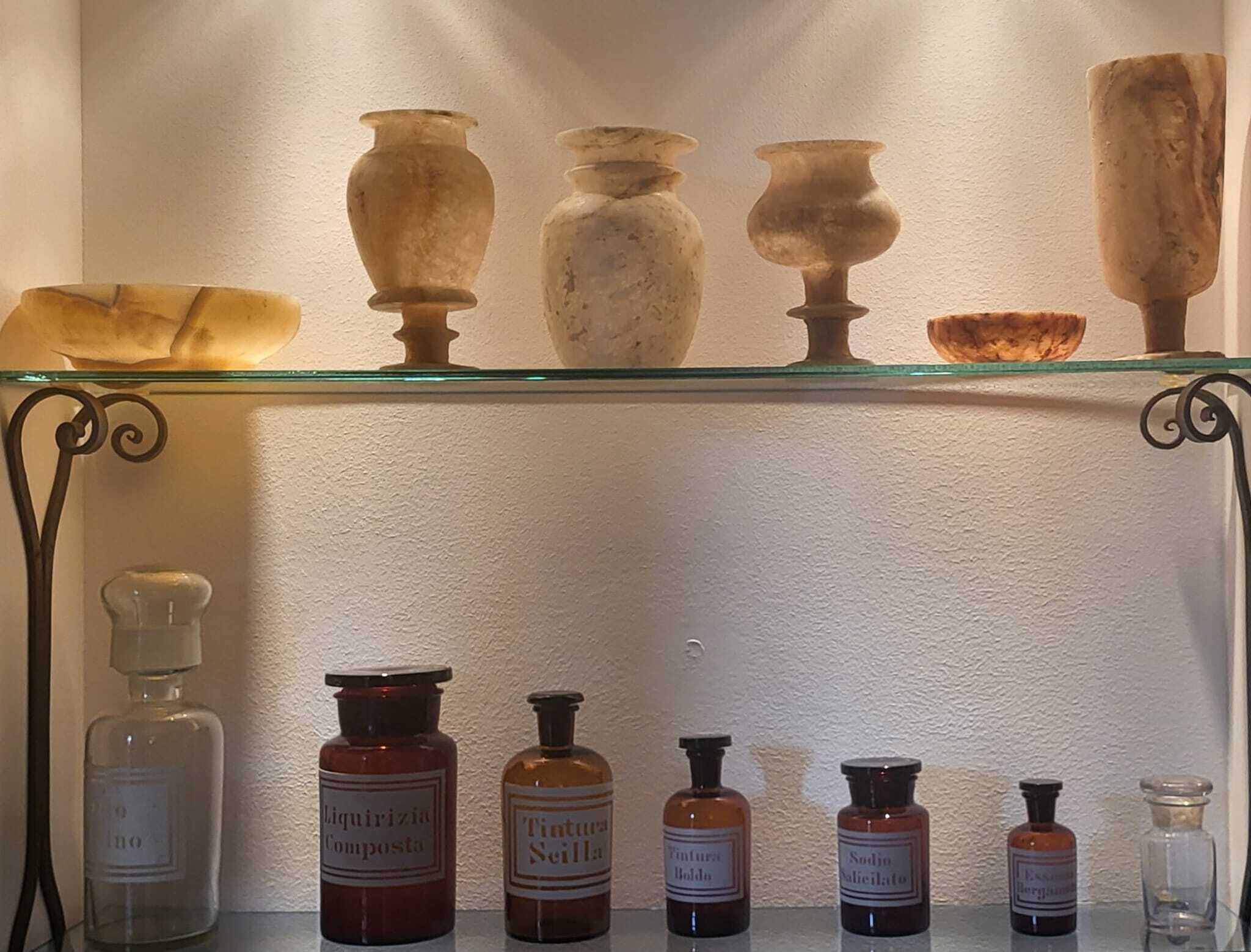 A shelf with antique vases and glass bottles labeled with various chemical names.