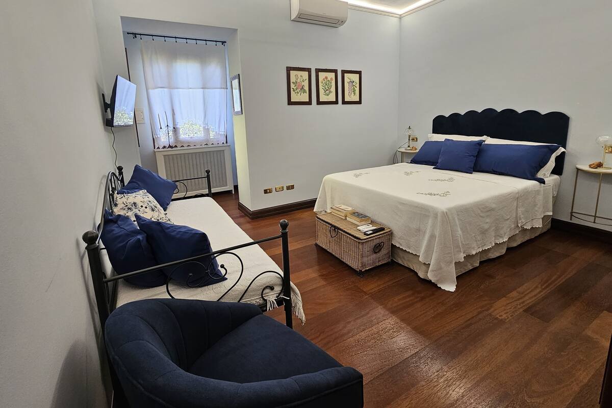 Un dormitorio con cama, mesita de noche, silla y ventana con cortinas.