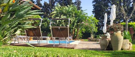 A pool area with two swing chairs, a small pool, and potted plants.