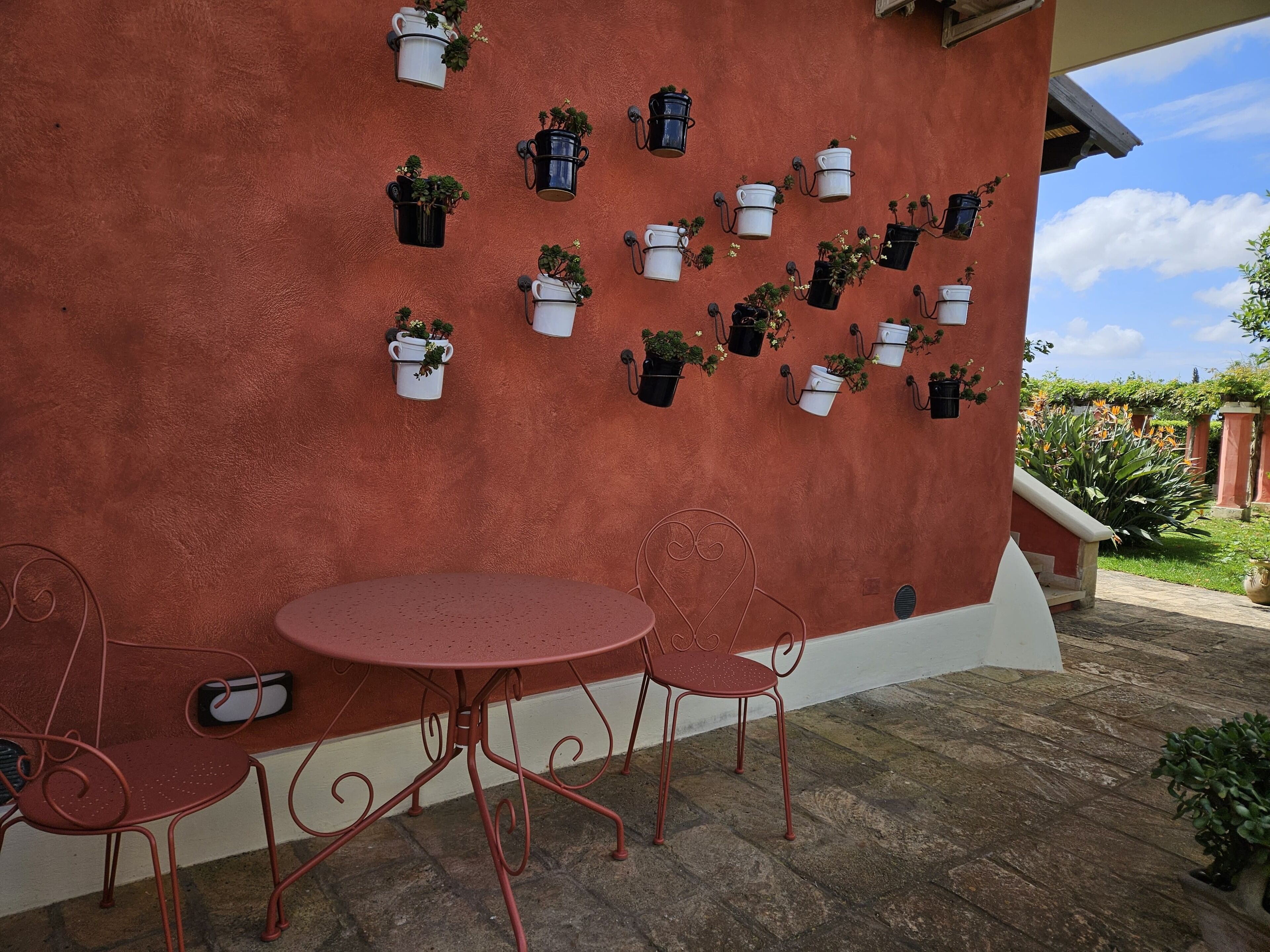A patio with a red wall, white columns, and a round table with two chairs.
