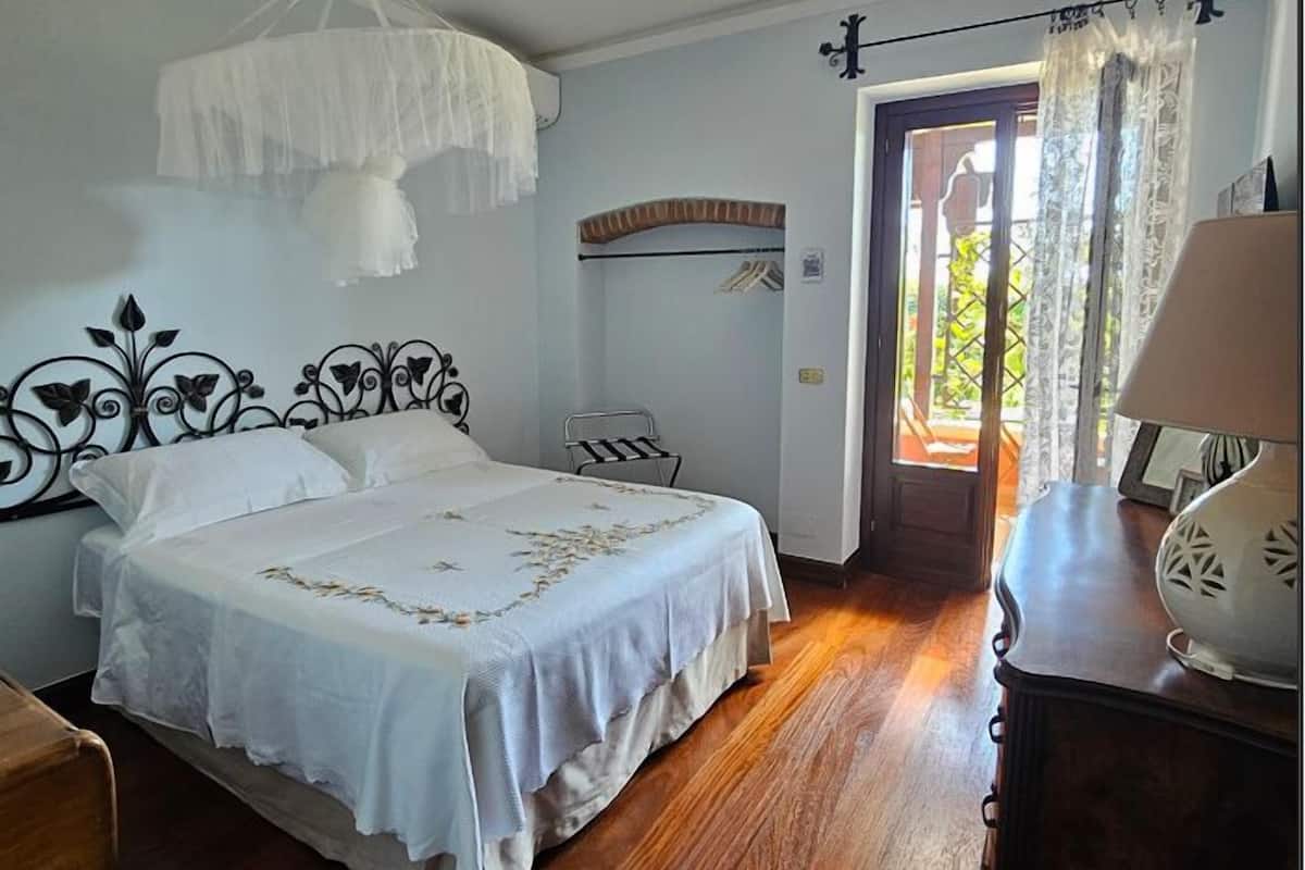 Un dormitorio con cama, ventilador de techo, mesita de noche y puerta que da al exterior.