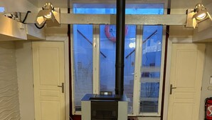 Een kamer met een houtkachel, witte deuren en een raam met zonwering.