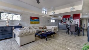 Een ruime woonkamer met een moderne keuken, een eethoek en een plafondventilator.