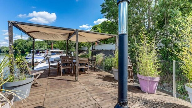 Een houten terras met buitenmeubilair, een overdekt gedeelte en uitzicht op boten op het water.