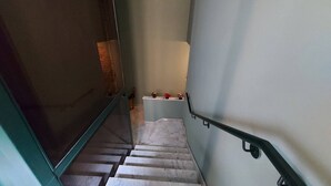 Una stretta scala con corrimano che conduce a un pianerottolo con una parete bianca e un piccolo ripiano con fiori.