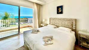 A hotel room with a large bed, a view of the sea, a balcony with a white fence, and a painting on the wall. - Villa Neptune Pour 8 Pieds Dans l eau Carthage (Carthage)