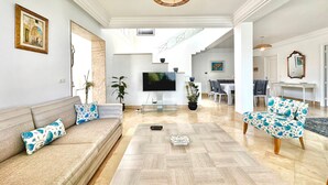 A spacious living room with a large wooden coffee table, a sofa with patterned cushions, a television, and a dining area with chairs and a table. - Villa Neptune Pour 8 Pieds Dans l eau Carthage (Carthage)