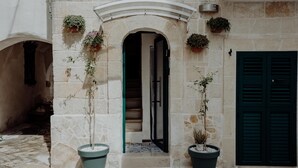 A stone building with a central archway, potted plants, and a dark green door. - Casa Viola - Palazzo Pezzola (Monopoli)