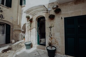 Une rue étroite bordée d’immeubles en pierre, avec des plantes en pot et un numéro de porte bien visible : le 47.