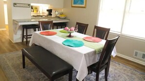 Een eetruimte met een tafel voor vier personen, een bankje en een keuken op de achtergrond.