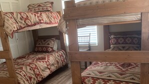 A dormitory room with two bunk beds, wooden flooring, and a window with blinds.