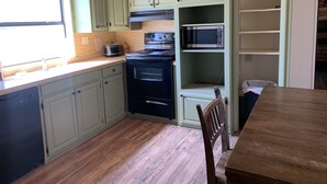 A kitchen with light green cabinets, a black stove, a microwave, and a wooden dining table.