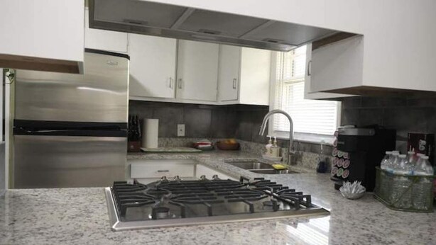 Una cocina moderna con un refrigerador de acero inoxidable, una estufa a gas y gabinetes blancos.