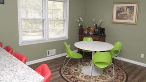 Un comedor con una mesa redonda, sillas verdes, un tapete estampado y una ventana con persianas.