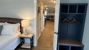 Et soveværelse med seng, natbord og lampe. Der er en gang, der fører til en opholdsstue med sofa og fjernsyn.