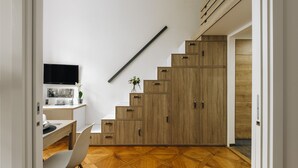 Une cuisine moderne avec un escalier en bois, un coin repas avec une chaise blanche et un téléviseur à écran plat fixé au mur.