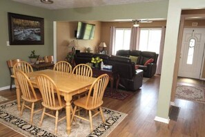 A dining area with a wooden table and chairs, a TV mounted on the wall, and a living room with a sofa and a fireplace. - Entire house in Metro Atlanta (Griffin)