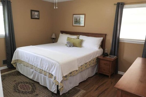 A neatly made bed with a white and yellow bedspread, a small bedside table with a lamp, and a framed picture on the wall.
