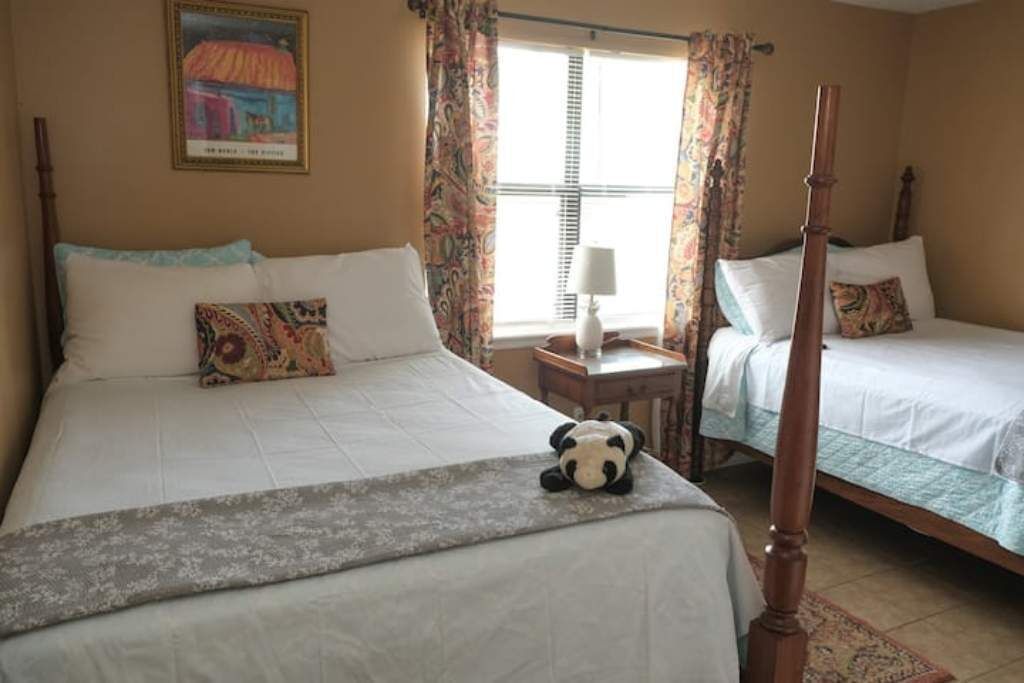 A hotel room with two beds, a nightstand, a lamp, and a window with curtains.