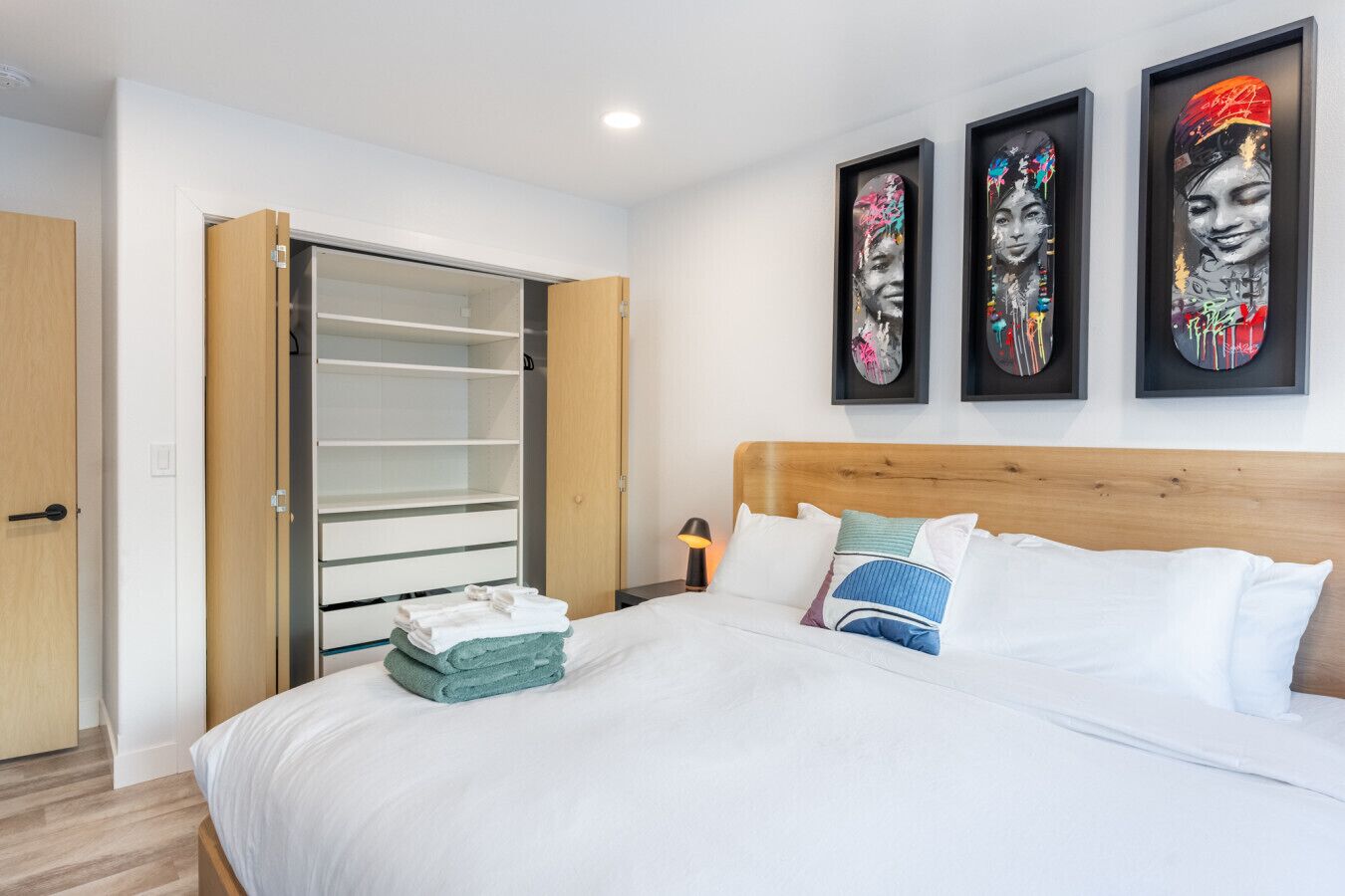 A hotel room with a bed, a wardrobe, and three framed artworks on the wall.