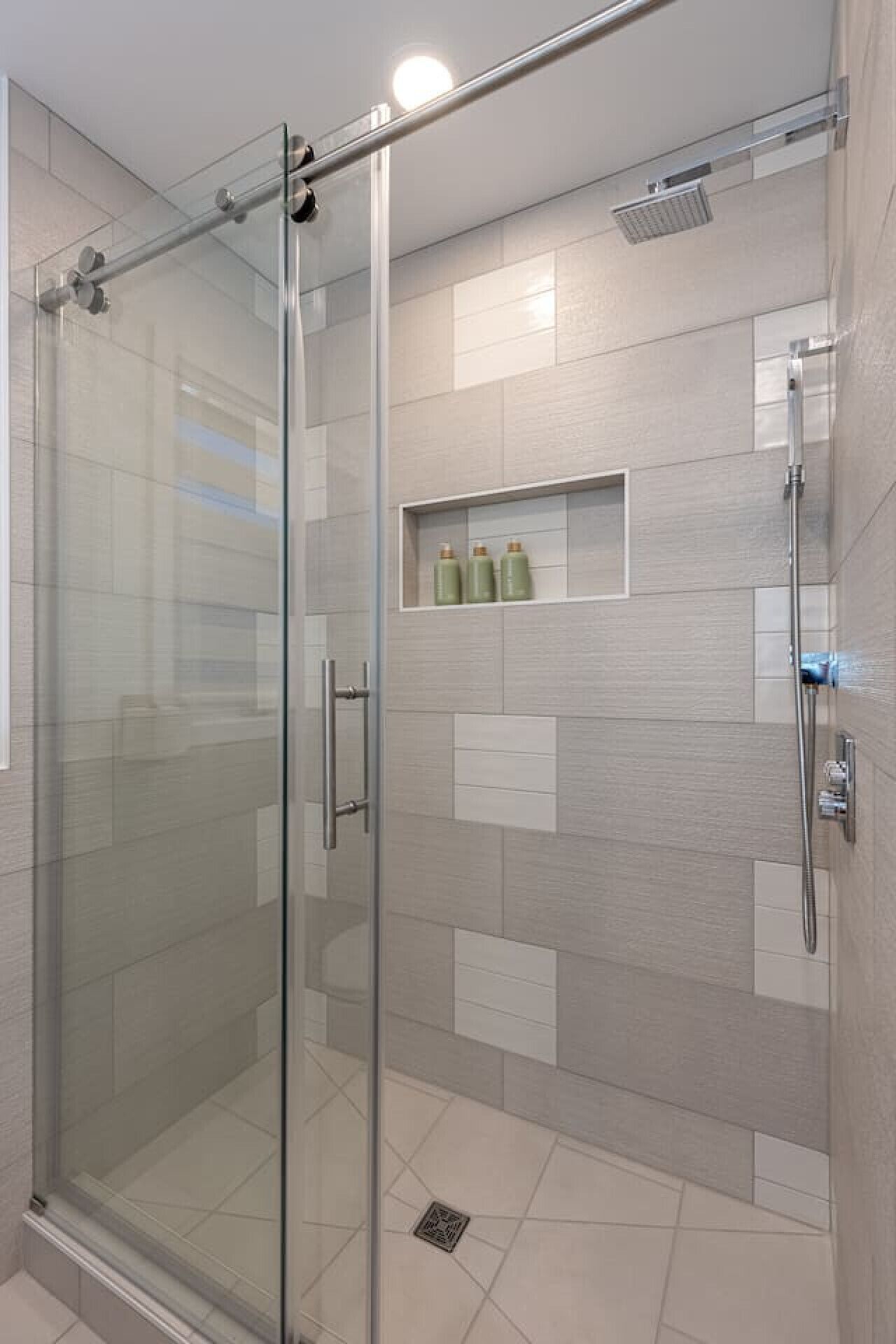 A glass-enclosed shower with a handheld showerhead and a wall-mounted control panel.
