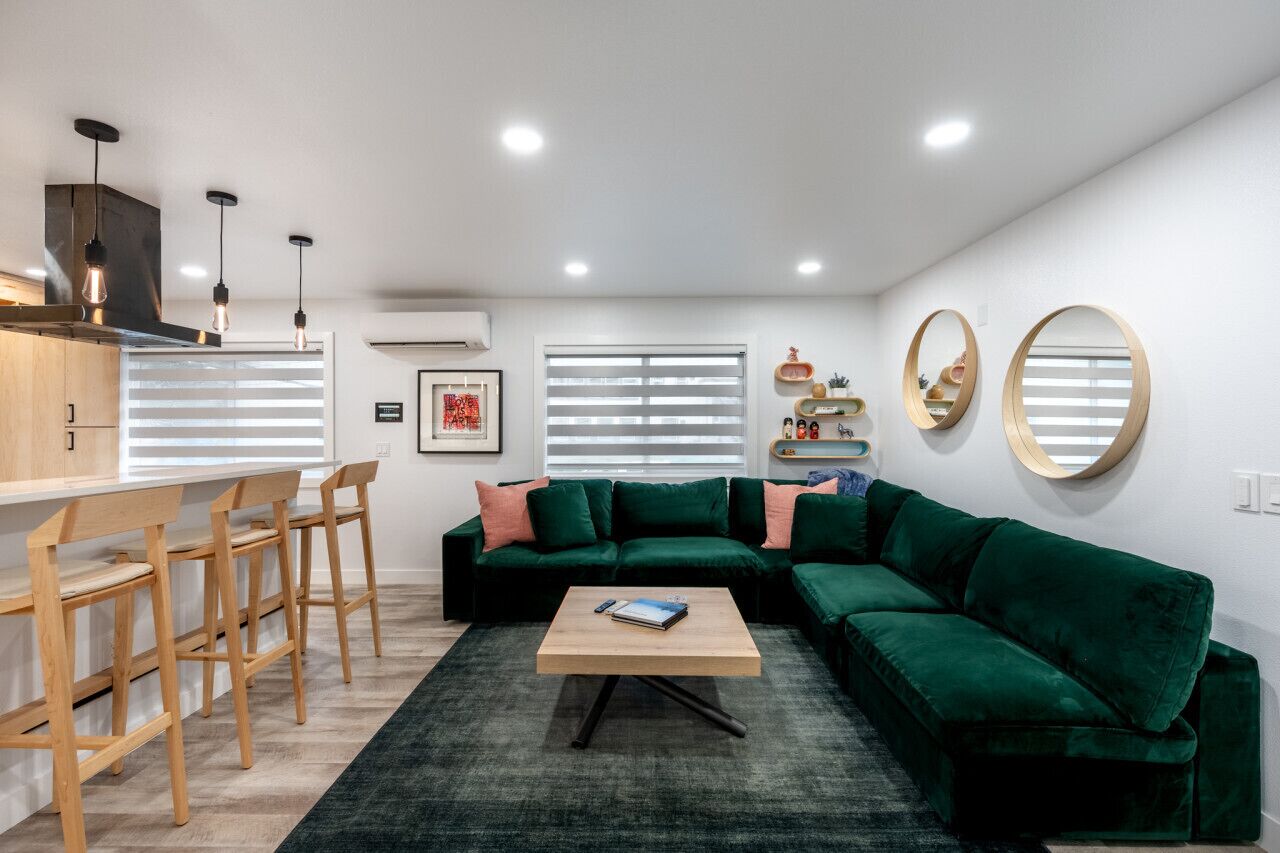 Ein modernes Wohnzimmer mit einem grünen Sofa, Holzstühlen, einem Couchtisch und einer Küchenzeile mit einer Bar.