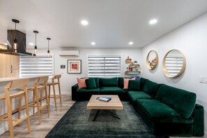 Un soggiorno moderno con un divano verde, sedie in legno, un tavolino da caffè e un angolo cottura con bancone.